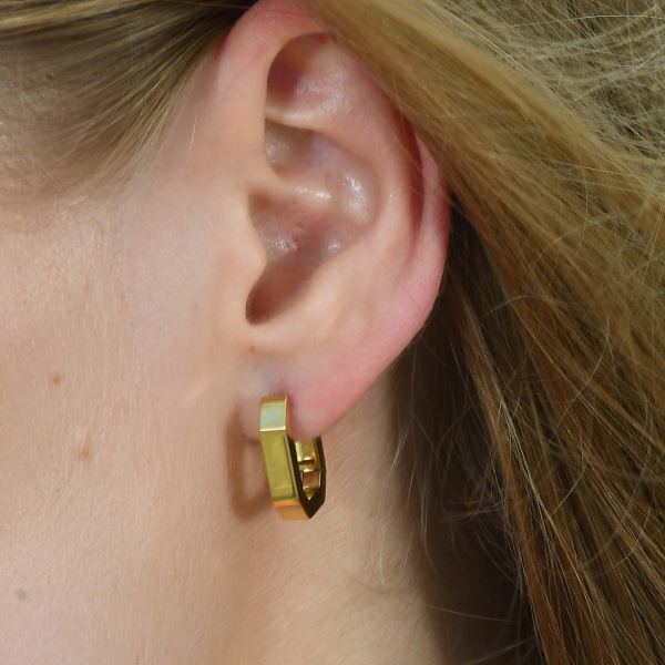 Show details for Octagon Hoop Earrings A close-up of a woman's ear wearing a single gold-plated octagon hoop earring, showcasing its modern, faceted, eight-sided design.